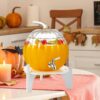 Seasonal pumpkin-shaped beverage dispenser with stainless steel tap and decorative wooden base.