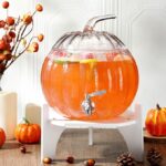 Pumpkin-shaped glass beverage dispenser with white wooden base and stainless steel spigot for parties.
