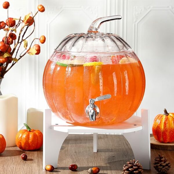 Pumpkin-shaped glass beverage dispenser with white wooden base and stainless steel spigot for parties.